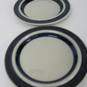 May include: Two ceramic plates with a cream-colored center and a dark blue border. The plates are round and have a simple, classic design. The plates are likely for serving food.