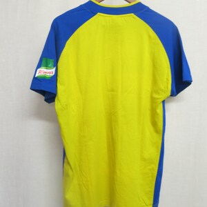 May include: Yellow and blue short-sleeved t-shirt with a green and red Knorr logo on the left sleeve.