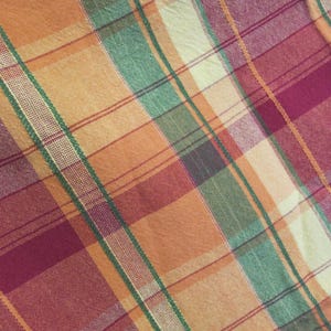 Könnte beinhalten: Nahaufnahme eines karierten Stoffes mit einer Mischung aus Farben. Das Muster weist sich kreuzende Linien in Orange-, Grün- und Burgundertönen auf, die ein klassisches Karomuster bilden. Der Stoff hat ein leicht strukturiertes Aussehen.
