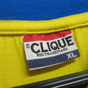 May include: A white tag with blue, red, and black trim. The tag says "CLIQUE REG. TRADEMARK" and "XL".