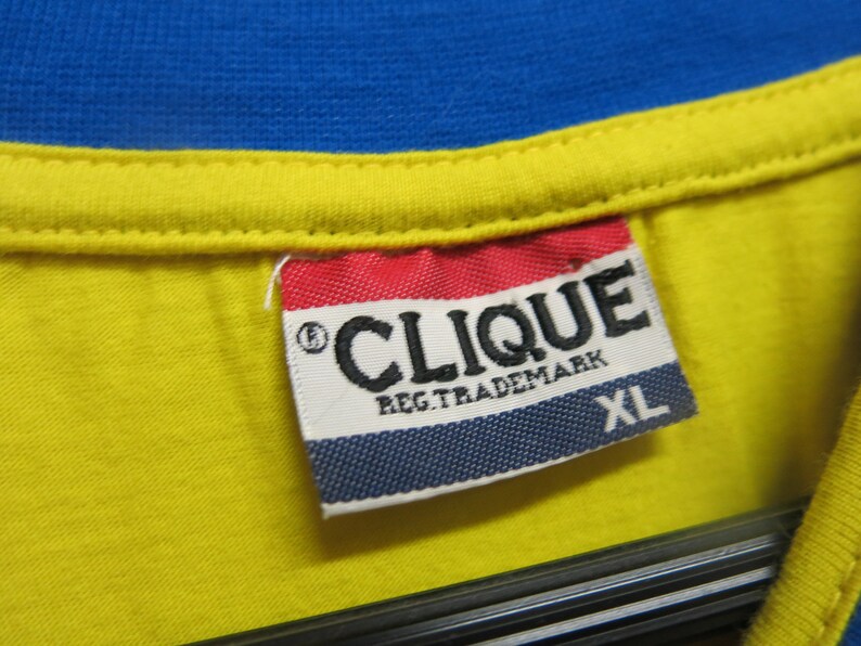 May include: A white tag with blue, red, and black trim. The tag says "CLIQUE REG. TRADEMARK" and "XL".