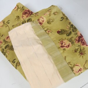 May include: A green fabric with a floral pattern of pink and red roses. The fabric is folded in half and has a cream-colored lining.