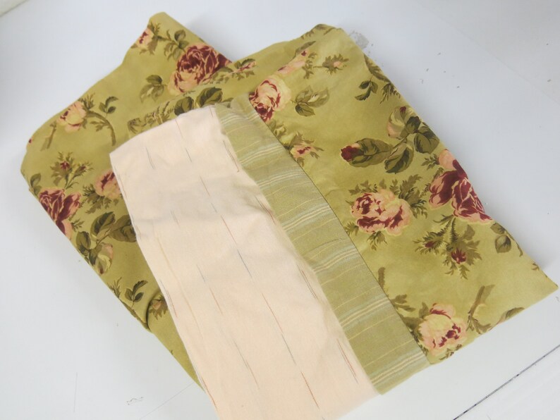 May include: A green fabric with a floral pattern of pink and red roses. The fabric is folded in half and has a cream-colored lining.