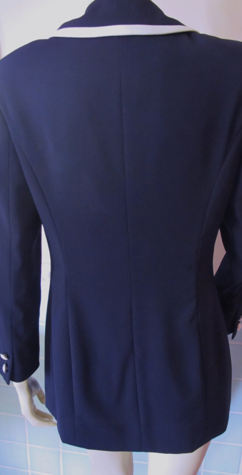 May include: A navy blue blazer with a white collar and trim. The blazer has a single button closure and long sleeves.