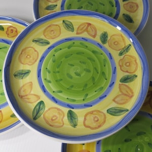May include: A set of decorative ceramic plates with a hand-painted floral design. Each plate features a yellow border with orange flower accents, green leaves, and a blue rim. The center has a green spiral design.