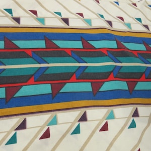 May include: A white fabric with a geometric pattern in shades of red, blue, teal, and gold. The pattern features triangles and arrows.