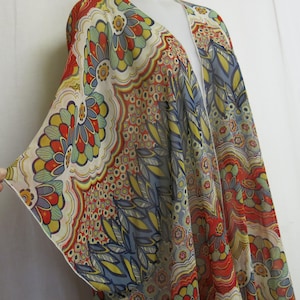 Könnte beinhalten: Ein langer, fließender Kimono mit einem farbenfrohen, abstrakten Blumenmuster in Rot-, Blau-, Gelb- und Grüntönen. Der Kimono ist aus einem durchsichtigen Stoff gefertigt und hat einen V-Ausschnitt.