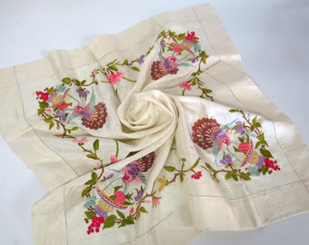 May include: A white linen tablecloth with embroidered floral designs in shades of pink, green, purple, and gold. The embroidery features birds and baskets of fruit.