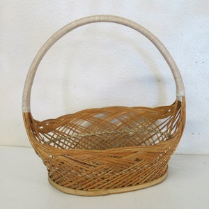 May include: A woven wicker basket with a white handle. The basket is oval shaped and has a woven pattern.