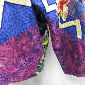 May include: A close-up of a quilted jacket with a patchwork design. The jacket is made of different fabrics with various patterns, including floral, seashells, and geometric designs. The fabric is a mix of blue, pink, and white.