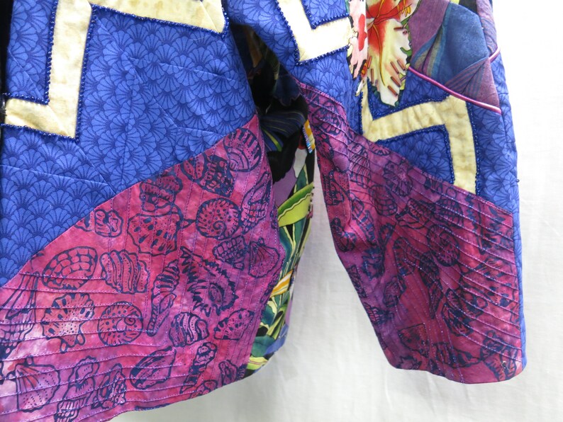 May include: A close-up of a quilted jacket with a patchwork design. The jacket is made of different fabrics with various patterns, including floral, seashells, and geometric designs. The fabric is a mix of blue, pink, and white.