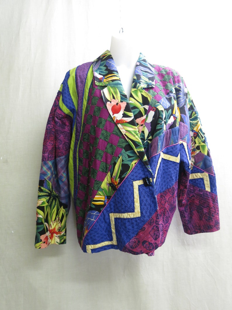 May include: A colorful patchwork jacket with a tropical print. The jacket has a collar and a button closure. The fabric is a mix of different textures and patterns, including floral, geometric, and abstract designs.