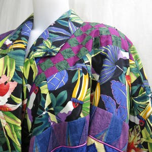 May include: A black, green, blue, and purple patchwork jacket with a tropical print featuring toucans and leaves. The jacket has a collar and a button closure.