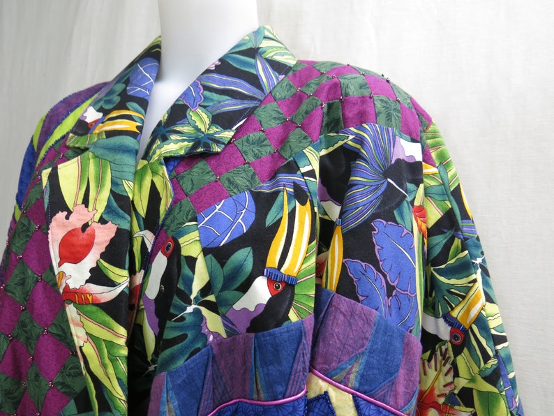 May include: A black, green, blue, and purple patchwork jacket with a tropical print featuring toucans and leaves. The jacket has a collar and a button closure.