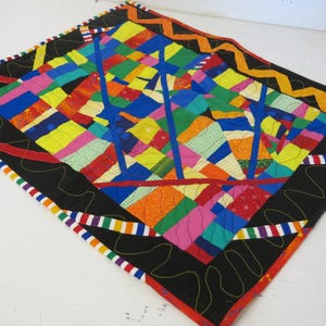 May include: A colorful patchwork quilt with a black border and a wavy, striped trim. The quilt is made of various fabrics in shades of red, orange, yellow, green, blue, and pink.