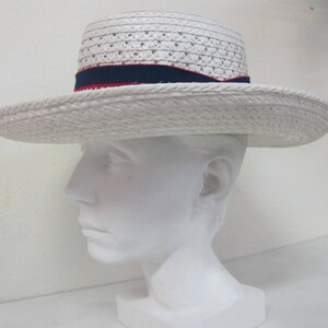 Puede incluir: Sombrero de paja blanco con una cinta roja y azul. El sombrero est&aacute; en una cabeza de maniqu&iacute; blanca.