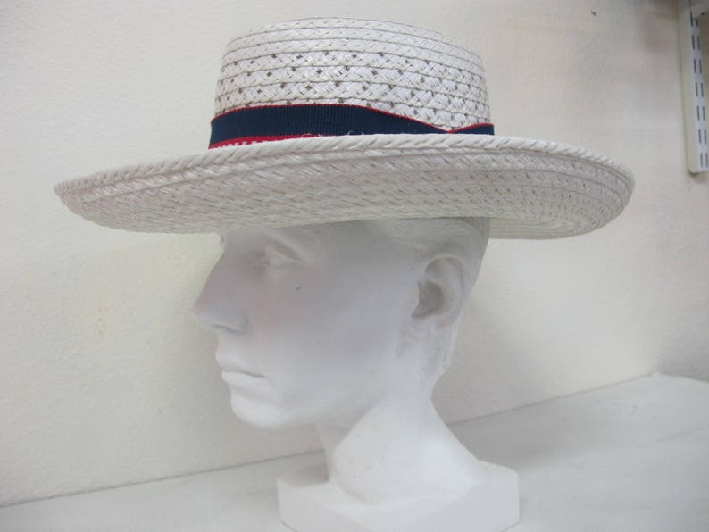 Puede incluir: Sombrero de paja blanco con una cinta roja y azul. El sombrero est&aacute; en una cabeza de maniqu&iacute; blanca.