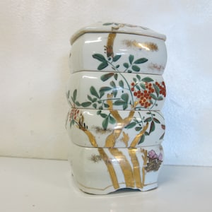 Pode incluir: Uma caixa de porcelana branca em camadas com um design floral dourado e verde. A caixa tem quatro camadas e é decorada com tinta vermelha, verde e dourada.