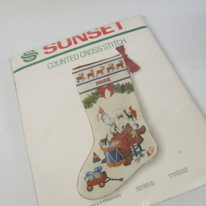 May include: A white counted cross stitch pattern for a Christmas stocking featuring Santa Claus with a drum and toys. The stocking is 14 inches long and includes a name space. The pattern is designed by Dan Trotter.