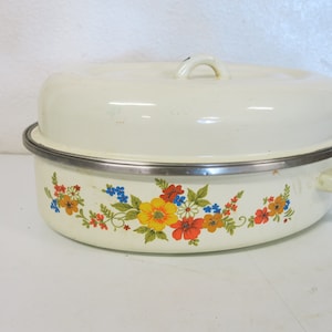 May include: White oval enamel roasting pan with a floral design in shades of orange, yellow, blue, and green. The pan has a lid with a silver rim and a handle.