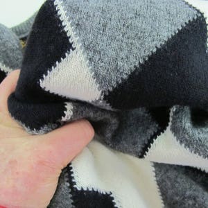 May include: A close-up of a black, white, and gray argyle sweater. The sweater is made of a soft, knitted fabric.