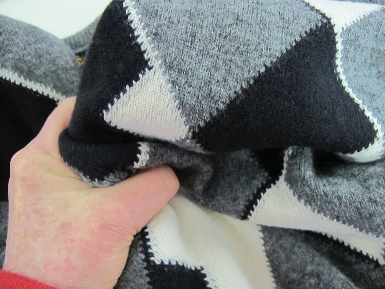 May include: A close-up of a black, white, and gray argyle sweater. The sweater is made of a soft, knitted fabric.