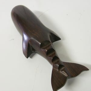 Op de afbeelding: Een donkerbruin houten walvisbeeld met een gegraveerde staart en een gladde, gepolijste afwerking.