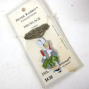 May include: Peter Rabbit Collection necklace with a 12-inch chain. The pendant features a colorful Peter Rabbit figure in a blue jacket, red gloves, and green leaves. The necklace is attached to a cardboard tag with the text "Peter Rabbit Collection Necklace".