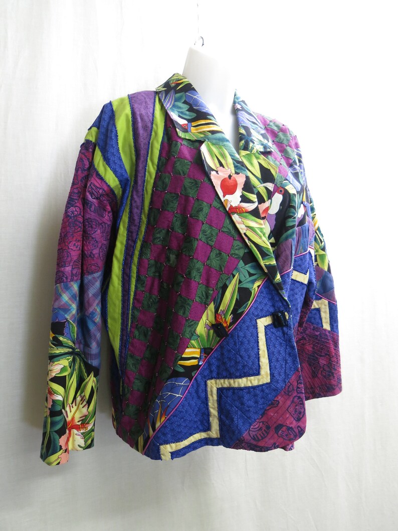 May include: A multi-colored patchwork jacket with a tropical print. The jacket has a green, purple, blue, and yellow color scheme. The jacket is made of different fabrics and has a quilted design.