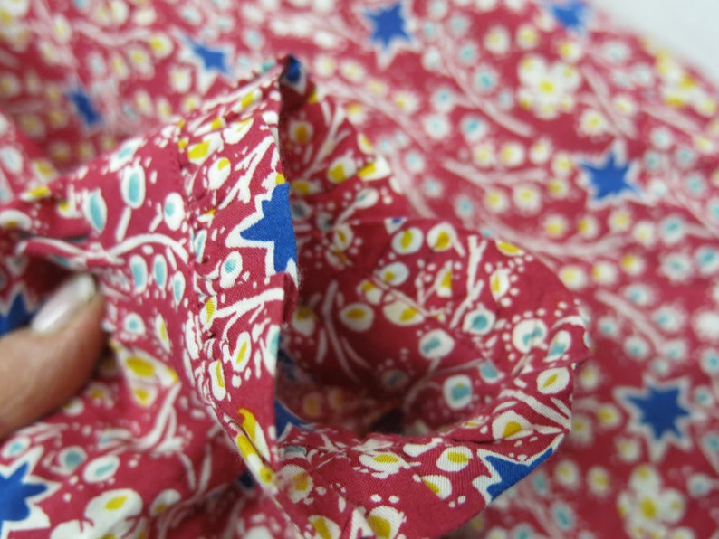 May include: Close-up of a red fabric with a white and blue floral pattern. The fabric has a ruffled edge.