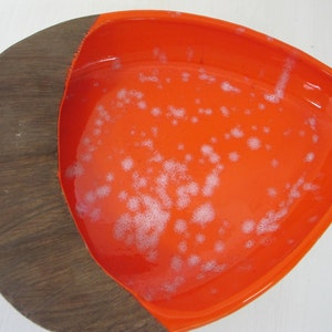 May include: A large, orange, ceramic serving dish with a wooden rim. The dish has a speckled, white glaze.