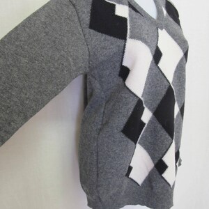 May include: A gray sweater with a black and white diamond pattern. The sweater has a V-neck and long sleeves.