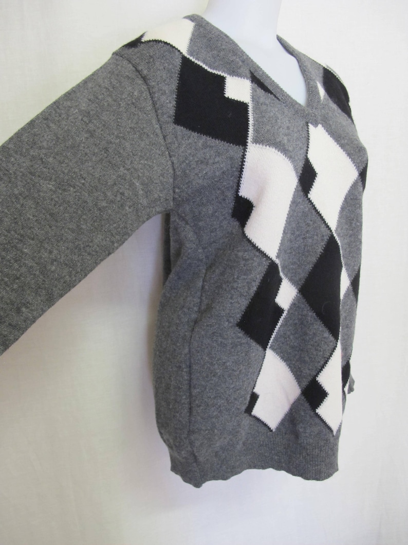 May include: A gray sweater with a black and white diamond pattern. The sweater has a V-neck and long sleeves.