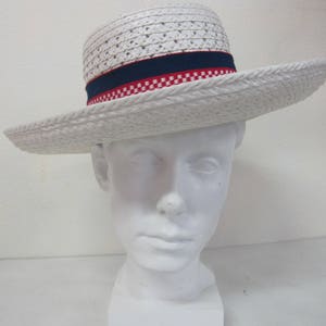 Puede incluir: Sombrero de paja blanco con una banda a cuadros azules y rojos. El sombrero est&aacute; en una cabeza de maniqu&iacute; blanca.