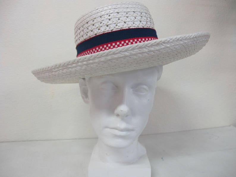 Puede incluir: Sombrero de paja blanco con una banda a cuadros azules y rojos. El sombrero est&aacute; en una cabeza de maniqu&iacute; blanca.