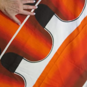May include: Abstract fabric with a white background and orange, brown, and black geometric shapes. The fabric has a gradient effect, with the orange fading to brown.