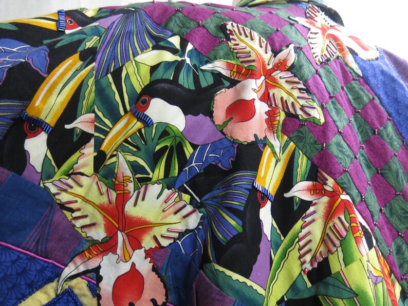 May include: A colorful fabric with a tropical print featuring toucans, orchids, and palm leaves. The fabric is a patchwork of different colors and patterns, including purple, green, blue, and yellow.