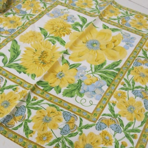 以下が含まれることがあります： 黄色と緑の花柄の白い布製のナプキン。模様には蝶、ひまわり、ぶどうが含まれています。ナプキンは黄色と緑の縁取りがされています。