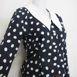 Op de afbeelding: Een marineblauwe blouse met witte stippen en een grote witte kraag. De blouse heeft een knoopsluiting aan de voorkant en lange mouwen.