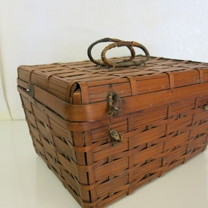 May include: A brown woven bamboo basket with a hinged lid and a woven handle. The basket has a metal clasp and a decorative metal piece on the front.