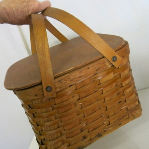 May include: A vintage wooden picnic basket with a woven wicker base and a hinged wooden lid. The basket has two leather handles and metal accents.