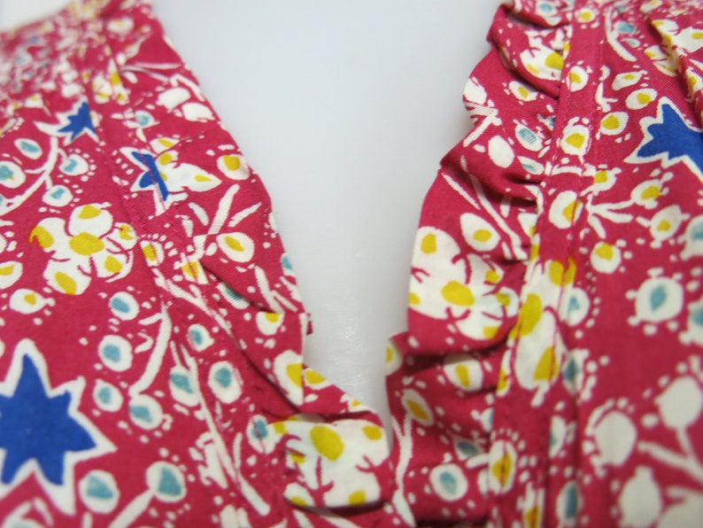 May include: Close-up of a pink fabric with a white floral and star pattern. The fabric has a ruffled edge.