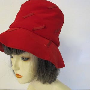 May include: A red felt hat with a wide brim and a unique design featuring red ribbon accents.