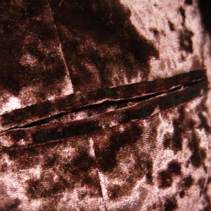 May include: Close-up of a brown velvet fabric with a subtle pink floral pattern. The fabric has a seam running horizontally across the image.