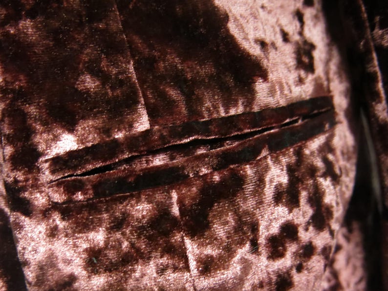 May include: Close-up of a brown velvet fabric with a subtle pink floral pattern. The fabric has a seam running horizontally across the image.
