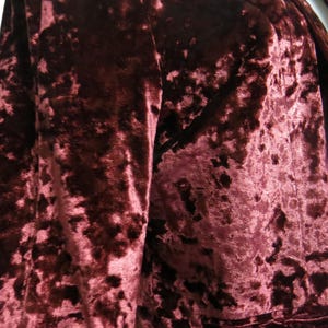 May include: A close-up of a burgundy crushed velvet blazer. The fabric has a textured, slightly raised pattern.
