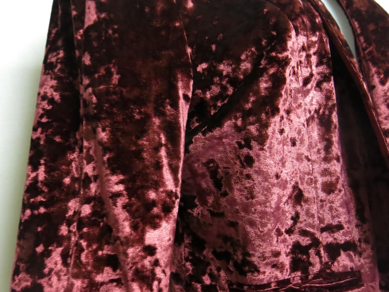 May include: A close-up of a burgundy crushed velvet blazer. The fabric has a textured, slightly raised pattern.