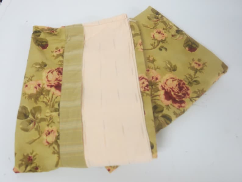 May include: Three pieces of fabric with a floral pattern. The fabric is green with pink and red roses. One piece of fabric has a striped pattern in green and white.