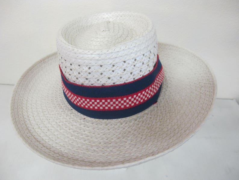 Puede incluir: Un sombrero de paja blanco con una banda a cuadros azules y rojos. El sombrero tiene un ala ancha y est&aacute; hecho de un material tejido.