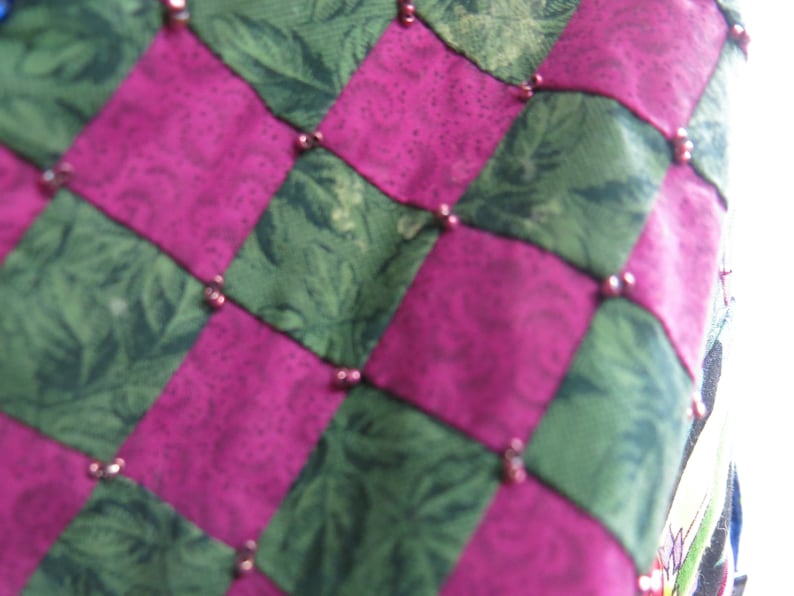 May include: A close-up of a pink and green patchwork quilt with a checkered pattern. The quilt is decorated with small, round beads.